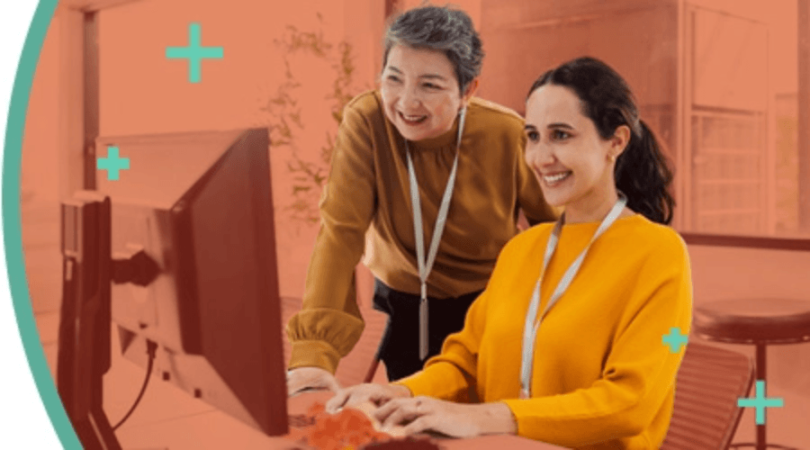 Two office workers, one sitting, the other standing, both looking at a computer screen.